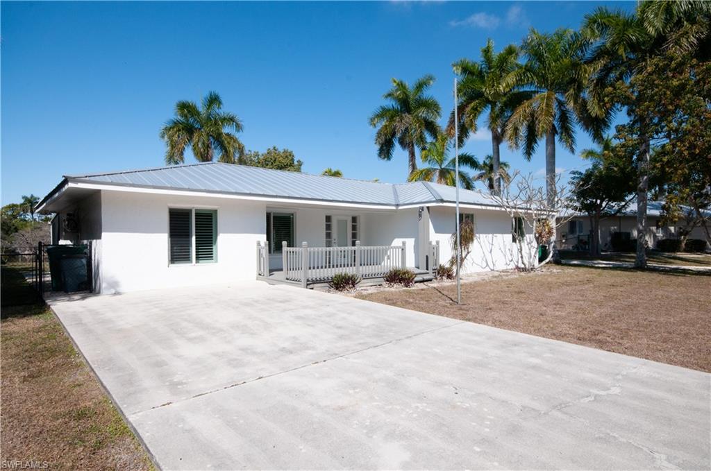 54 Liberty Lane Naples, FL 34112 - Photo 2 of 30 Ranch-style house with stucco siding, a metal roof, a front yard, driveway, and a porch