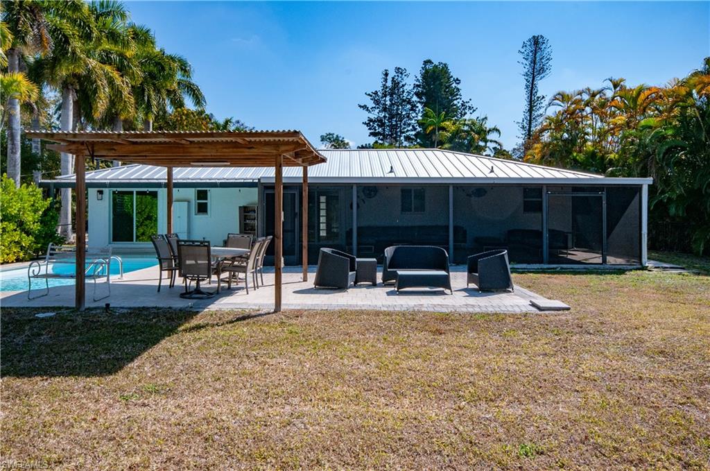 54 Liberty Lane Naples, FL 34112 - Photo 28 of 30 Rear view of house with a pergola, a yard, a patio area, an outdoor pool, and a metal roof