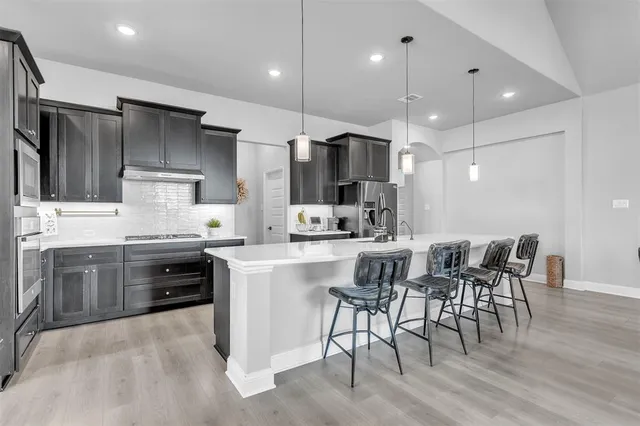 a kitchen with stainless steel appliances kitchen island granite countertop a sink a stove a refrigerator cabinets and chairs