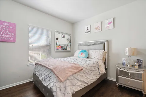 a bedroom with a bed and a lamp on dresser with wooden floor