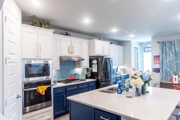 a kitchen with granite countertop a refrigerator a stove a sink dishwasher and white cabinets with wooden floor