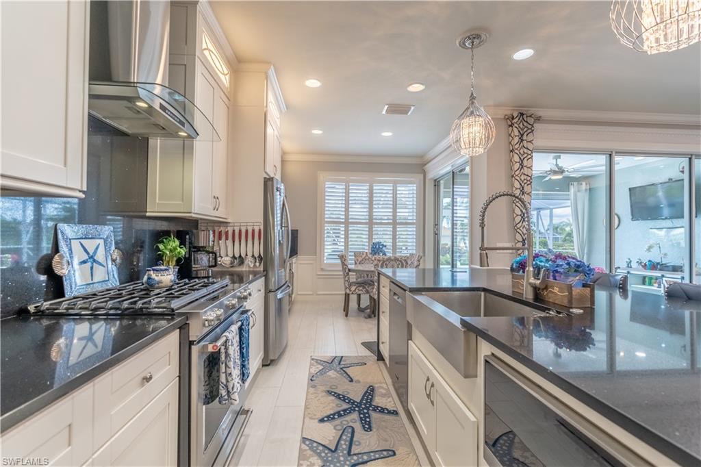 8883 Ravello Court Naples, FL 34114 - Photo 15 of 35 Kitchen with wall chimney range hood, stainless steel appliances, ceiling fan with notable chandelier, ornamental molding, and backsplash