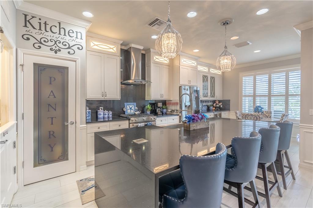 8883 Ravello Court Naples, FL 34114 - Photo 16 of 35 Kitchen featuring tasteful backsplash, wall chimney range hood, hanging light fixtures, high end range, and an island with sink