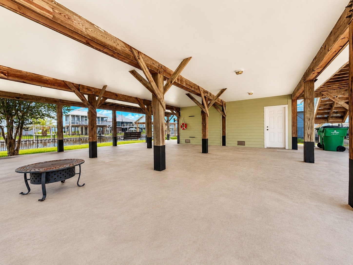 135 Sand Shoals Road Freeport, TX 77541 - Photo 5 of 20 This photo showcases a spacious, covered outdoor area with sturdy wooden beams and a concrete floor. It includes a small fire pit and provides ample open space, ideal for gatherings or parking. The area is surrounded by a fence, with nearby houses visible, suggesting a residential neighborhood setting.