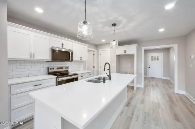 a kitchen with stainless steel appliances a microwave a stove a sink dishwasher a refrigerator white cabinets and wooden floor