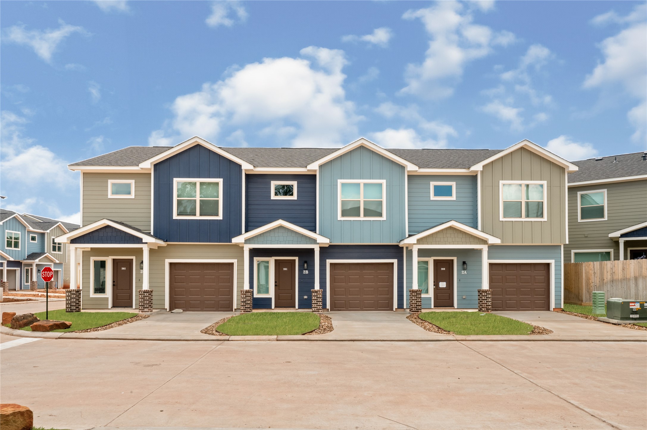 14010 Longstreet Road, Unit 2 Willis, TX 77318 - Photo 1 of 29 Modern townhouse with a two-story design and attached garages. The exterior features a blend of blue and beige siding with white accents, creating a clean and inviting look. The property is part of a neatly arranged complex, offering a suburban feel with well-maintained lawns and a quiet street setting.