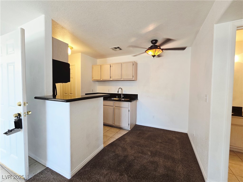 5211 South Lindell Road, Unit 104 Las Vegas, NV 89118 - Photo 4 of 12 Kitchen with light tile patterned flooring, light brown cabinetry, dark countertops, a textured ceiling, and light colored carpet
