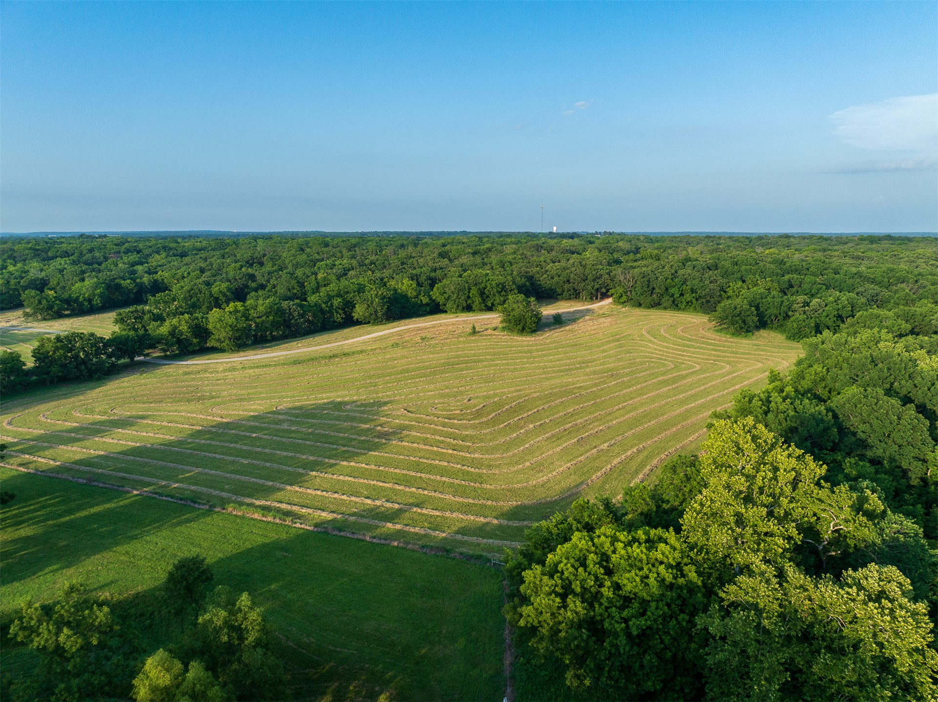 15291 East 400 Road Claremore, OK 74017 - Photo 74 of 96 Expansive open field with mown patterns, surrounded by dense mature trees, and a clear sky backdrop