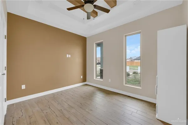 an empty room with wooden floor chandelier fan and windows