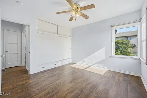 an empty room with wooden floor fan and windows