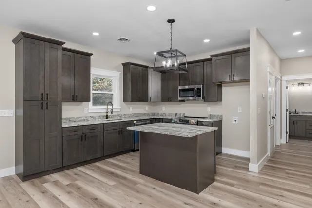 a kitchen with kitchen island granite countertop stainless steel appliances lots of counter top space refrigerator and cabinets