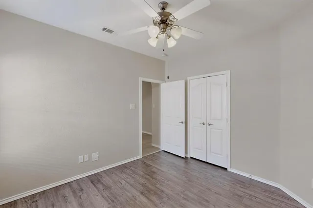 a view of an empty room with chandelier fan and wooden floor