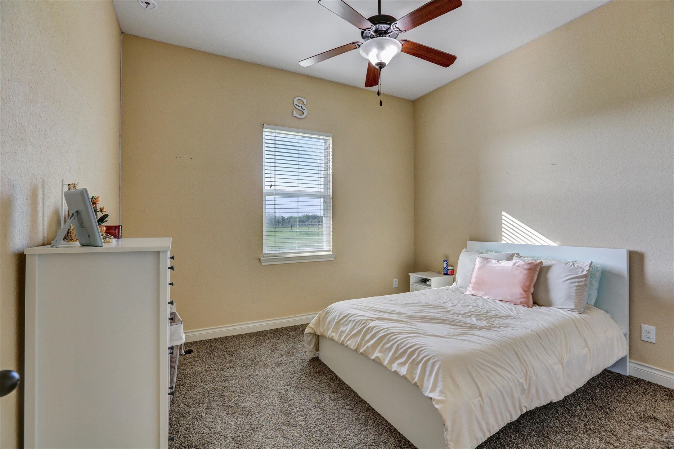 8131 Brinkmeyer Road Needville, TX 77461 - Photo 21 of 49 Cozy bedroom with soft carpeting, a ceiling fan, and natural light streaming through the window, creating a serene and inviting atmosphere.