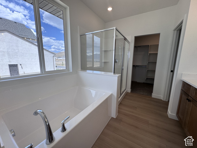 2613 Scarlet Road, Unit 258 Eagle Mountain, UT 84005 - Photo 15 of 30 Soaking tub with chrome fixtures, glass-enclosed shower, wood-finish flooring, built-in closet shelving, and a vanity with a white countertop