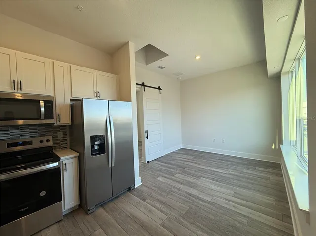 a view of a kitchen with wooden floor electronic appliances and windows