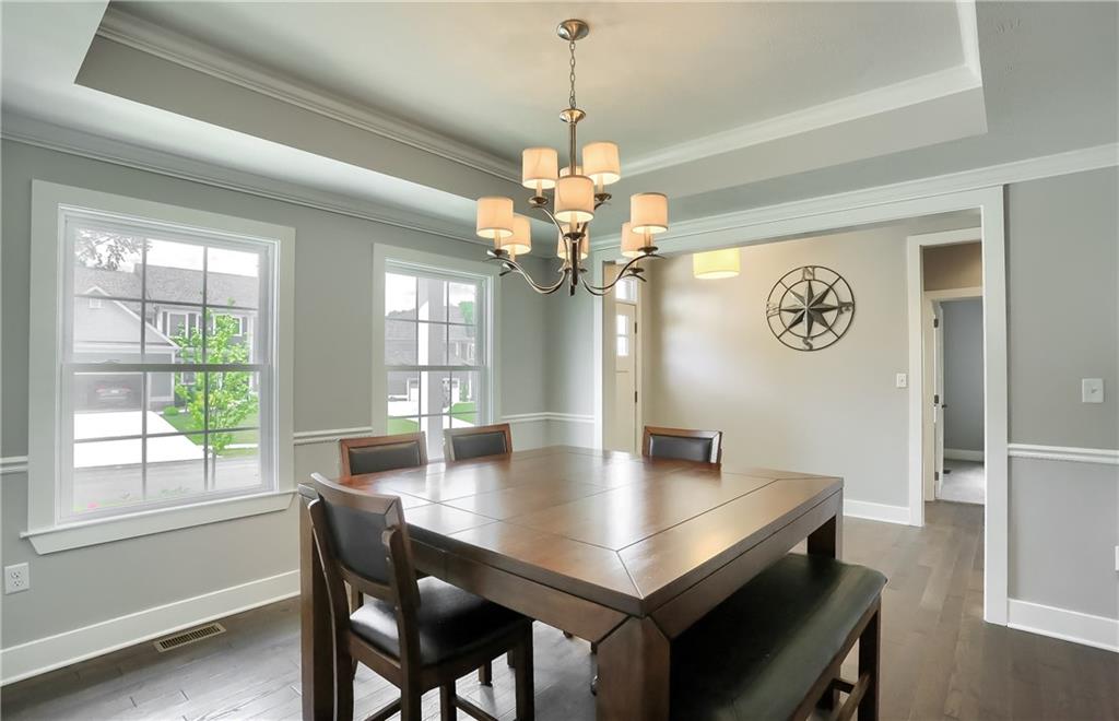 Sprawling hardwood flooring flows into the elegant dining room with crown molding, a chair rail, trey ceiling, and modern tone.