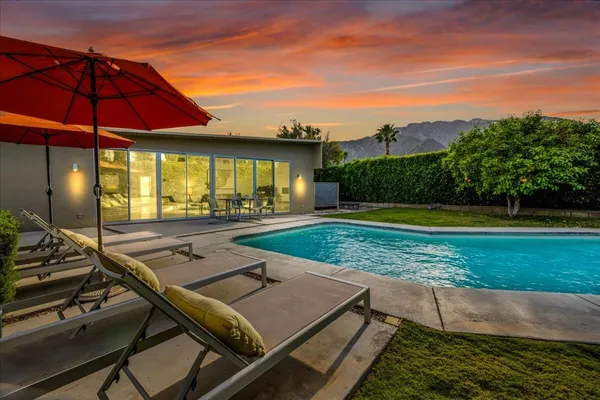 a view of pool with lawn chairs under an umbrella