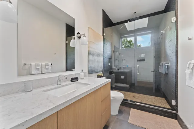a bathroom with a granite countertop sink a toilet a mirror and shower