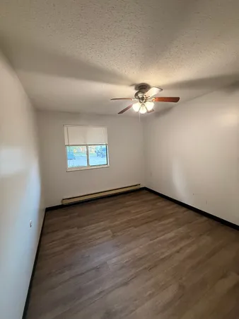 an empty room with wooden floor chandelier fan and windows