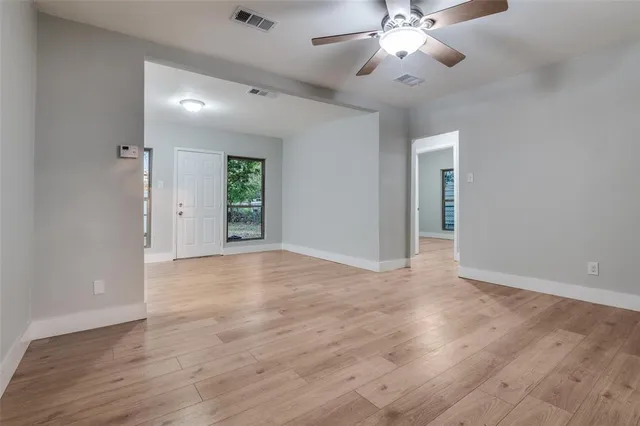 a view of an empty room with chandelier fan and wooden floor