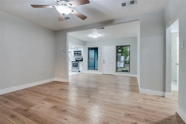 a view of an empty room with wooden floor and a ceiling fan