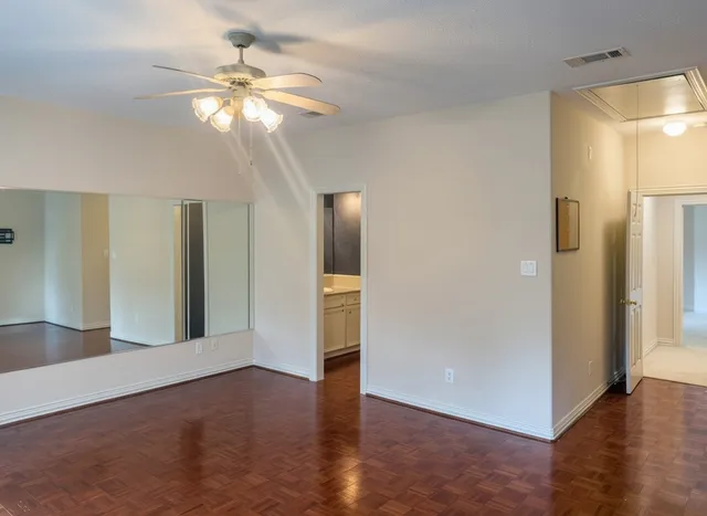 a view of an empty room with wooden floor and a ceiling fan