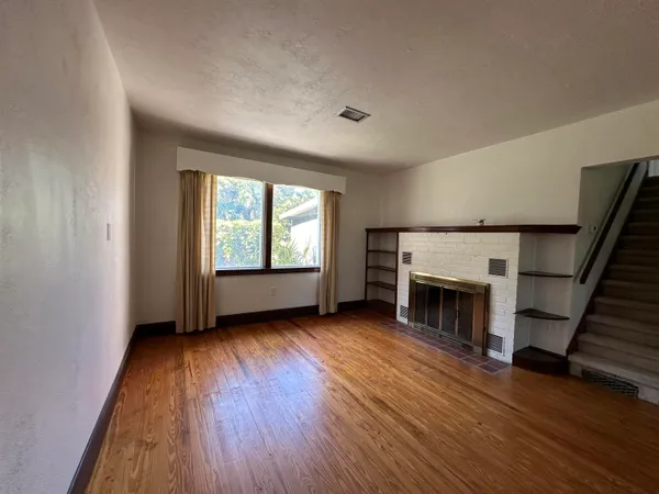 an empty room with wooden floor fireplace and windows