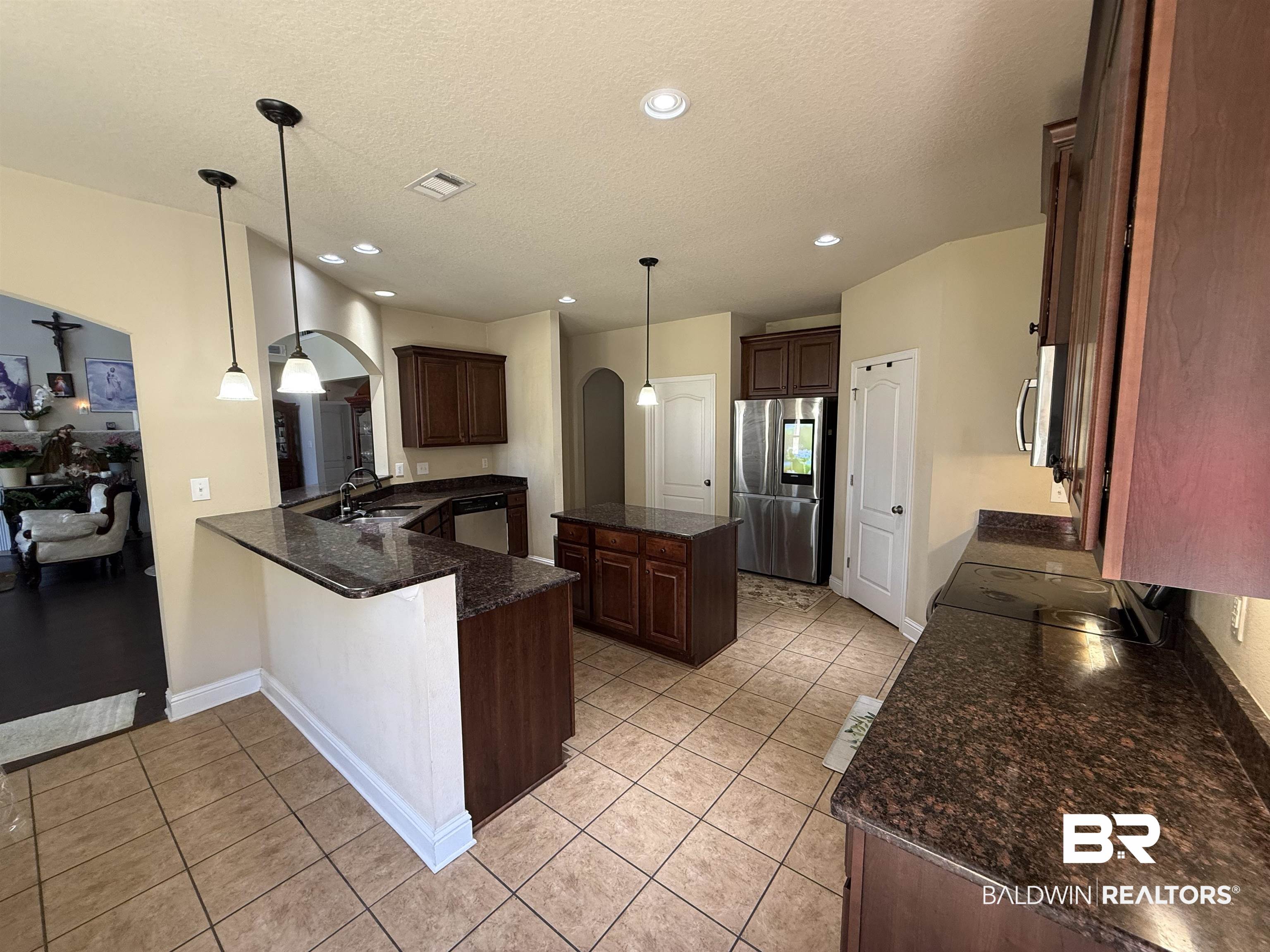 9023 Krystal Ridge Court Daphne, AL 36526 - Photo 13 of 41 Kitchen with arched walkways, a center island, appliances with stainless steel finishes, light tile patterned floors, and dark brown cabinets