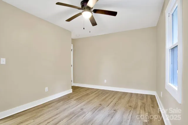 an empty room with wooden floor chandelier fan and windows