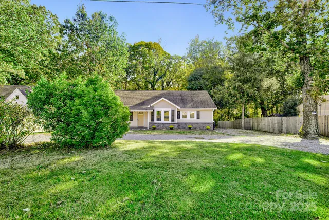 a house that is sitting in the grass with large trees and plants