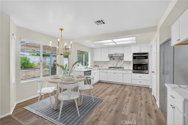 a kitchen with stainless steel appliances granite countertop a stove top oven a sink dishwasher and white cabinets with wooden floor