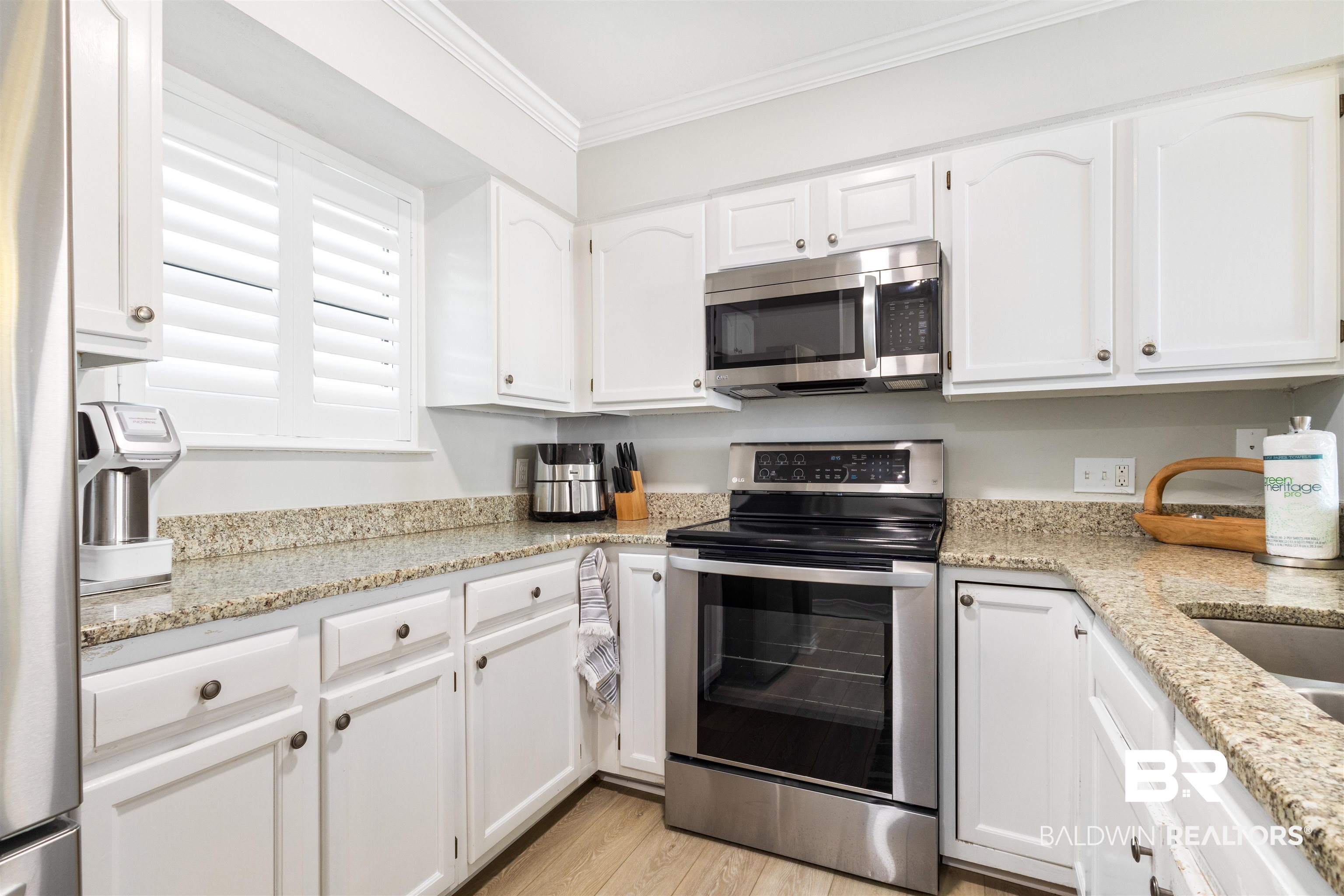 25861 Canal Road, Unit 3 Orange Beach, AL 36561 - Photo 7 of 40 Kitchen featuring appliances with stainless steel finishes, white cabinetry, light stone counters, crown molding, and light wood-type flooring