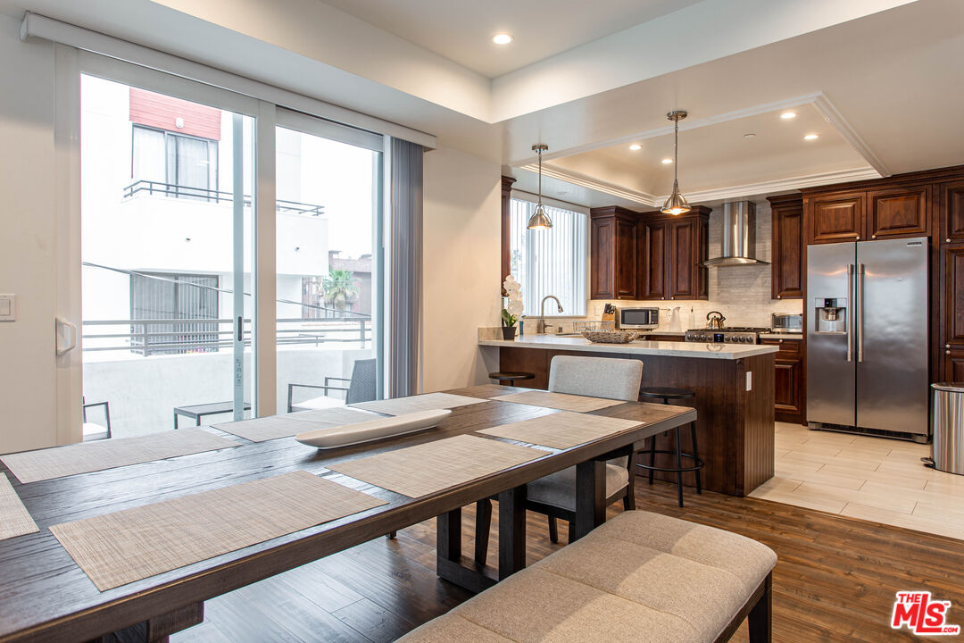 a kitchen with stainless steel appliances granite countertop a stove a refrigerator a sink a dining table and chairs with wooden floor