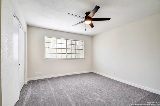 an empty room with ceiling fan and windows