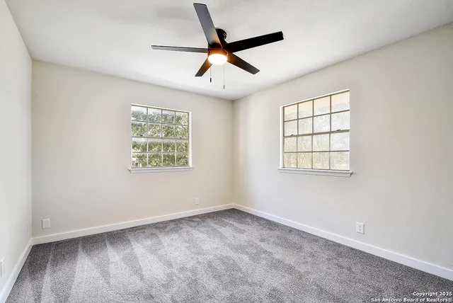an empty room with ceiling fan and windows