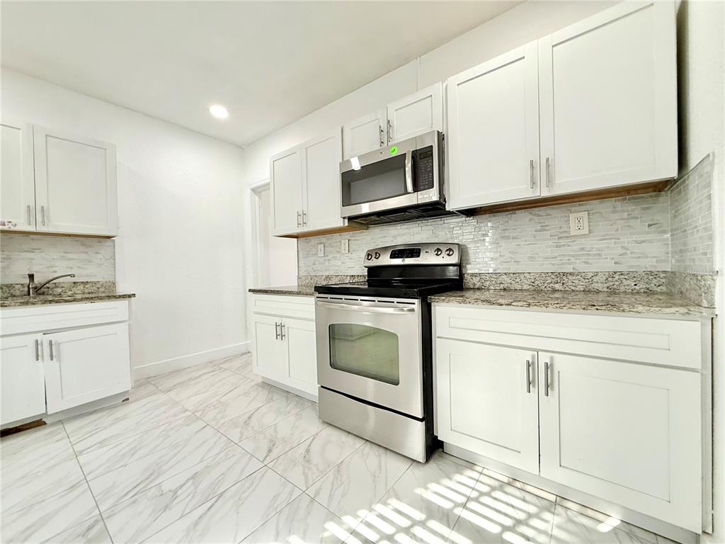 507 North Ridgewood Avenue, Unit 4 Daytona Beach, FL 32114 - Photo 4 of 7 a kitchen with stainless steel appliances granite countertop white cabinets a sink a stove a microwave and a refrigerator