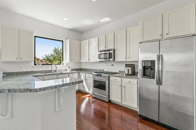 a kitchen with stainless steel appliances granite countertop a refrigerator a stove a sink and white cabinets with wooden floor