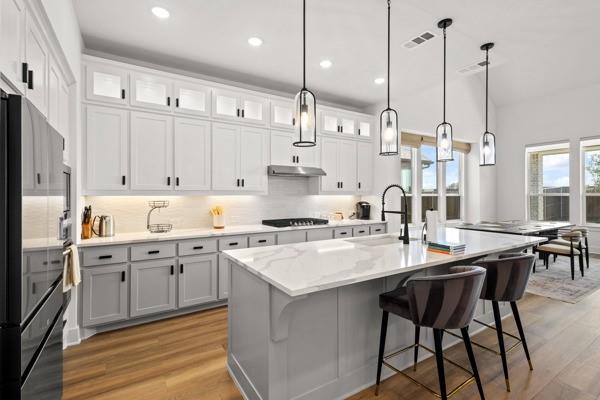 1825 Rough Rdg Trail Midlothian, TX 76065 - Photo 9 of 37 Gourmet kitchen featuring a large island with white stone countertop, two-tone cabinetry with matte black hardware, wood-finish flooring, recessed lighting, and modern pendant fixtures