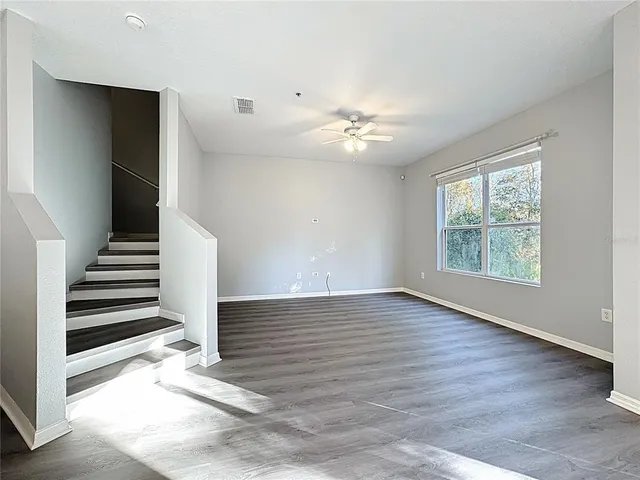 an empty room with wooden floor chandelier fan and windows