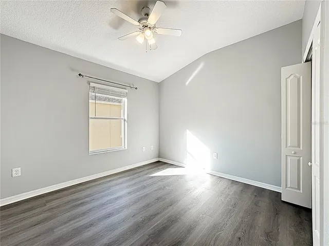 an empty room with wooden floor fan and windows