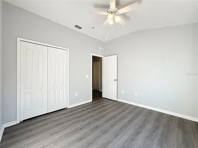 an empty room with wooden floor chandelier fan and windows