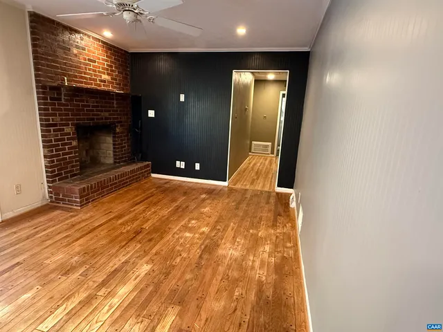 a view of an empty room with wooden floor and a fireplace