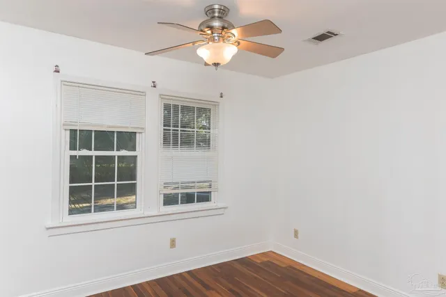 an empty room with wooden floor chandelier fan and windows