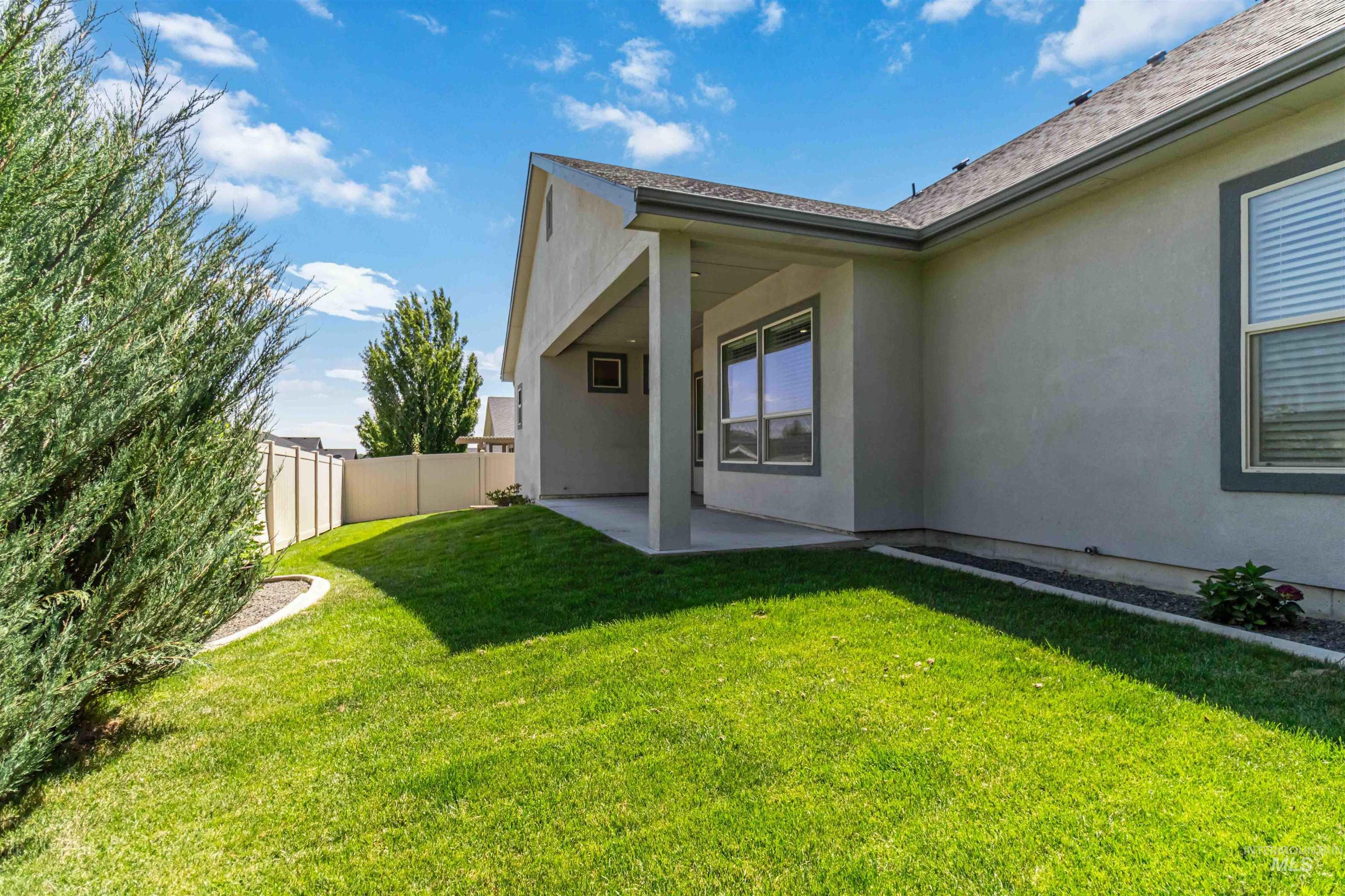 3218 North Cherry Laurel Way Star, ID 83669 - Photo 47 of 50 Expansive rear yard featuring a manicured lawn, established landscaping, a covered patio, and a gravel side path leading to a privacy-fenced gate