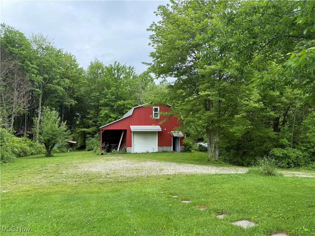 5595 Ford Road Madison, OH 44057 - Photo 17 of 36 View of green lawn featuring driveway, an outdoor structure, a garage, a pole building, and a forest view