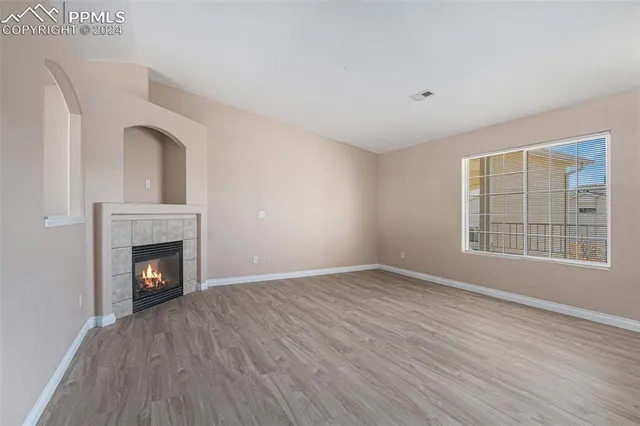 a view of an empty room with wooden floor fireplace and a window