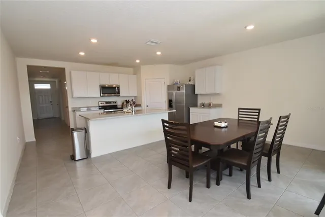 a kitchen with stainless steel appliances kitchen island granite countertop a table chairs and a refrigerator