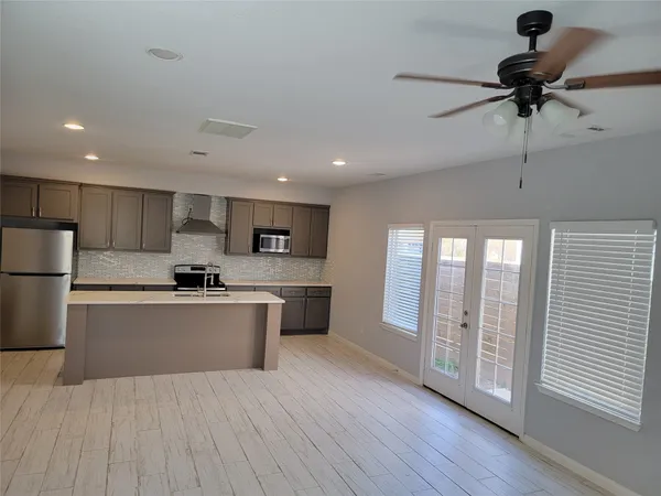 a large kitchen with stainless steel appliances a large counter top a refrigerator and cabinets