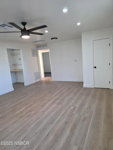 a view of an empty room with wooden floor and a ceiling fan