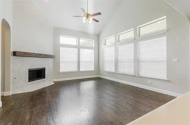 a view of an empty room with wooden floor fireplace and a window